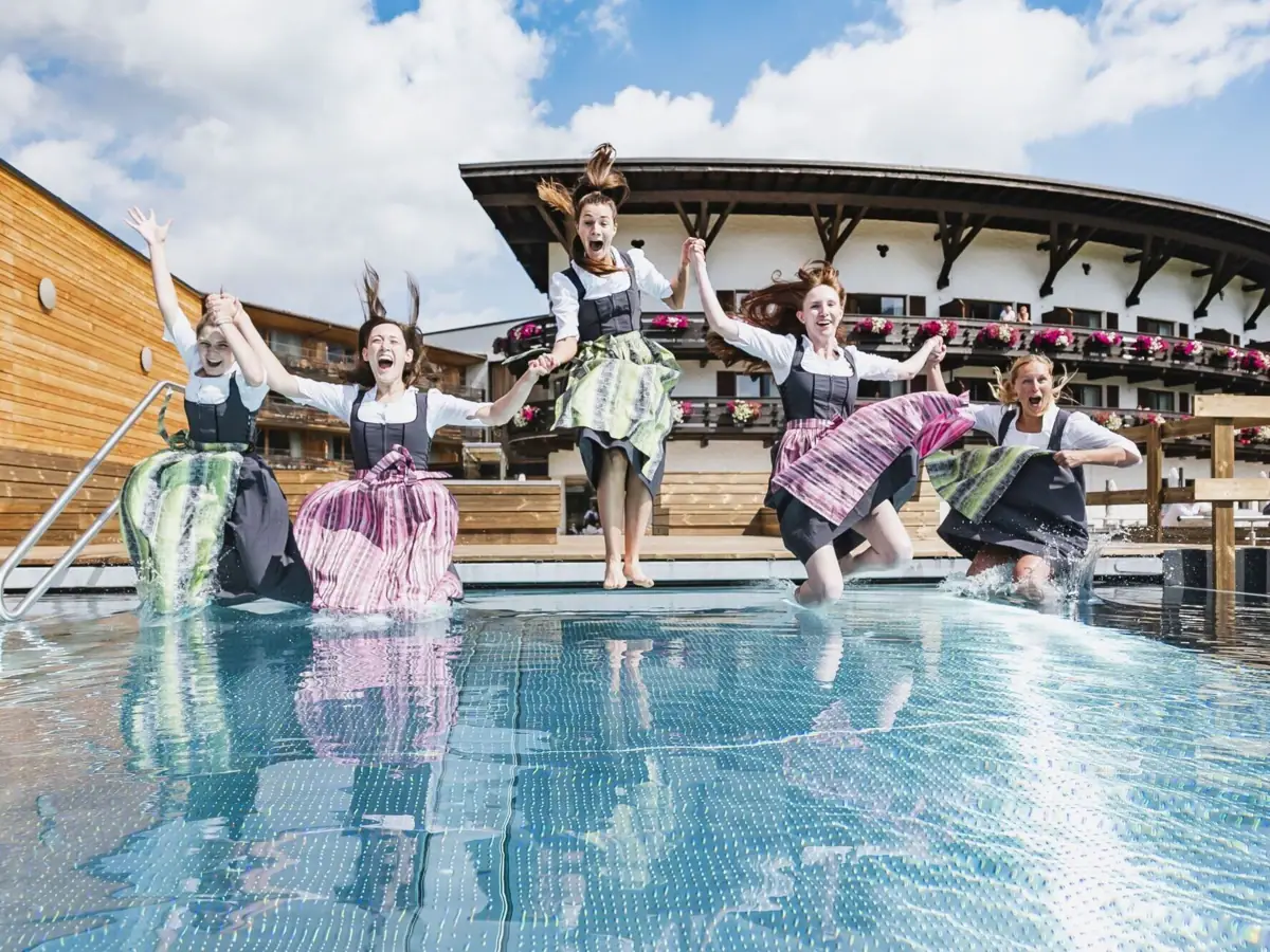 Eine Gruppe von Frauen mit Dirndln springt in einen Pool.