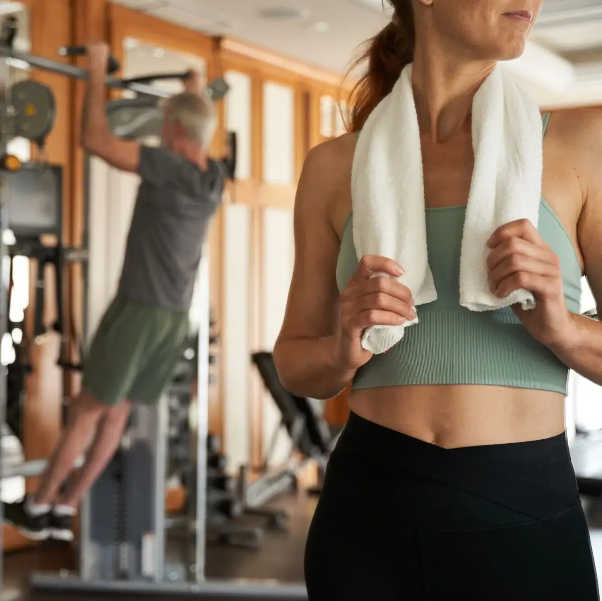 Eine Frau im Fitnessstudio hält ein Handtuch um ihren Nacken.