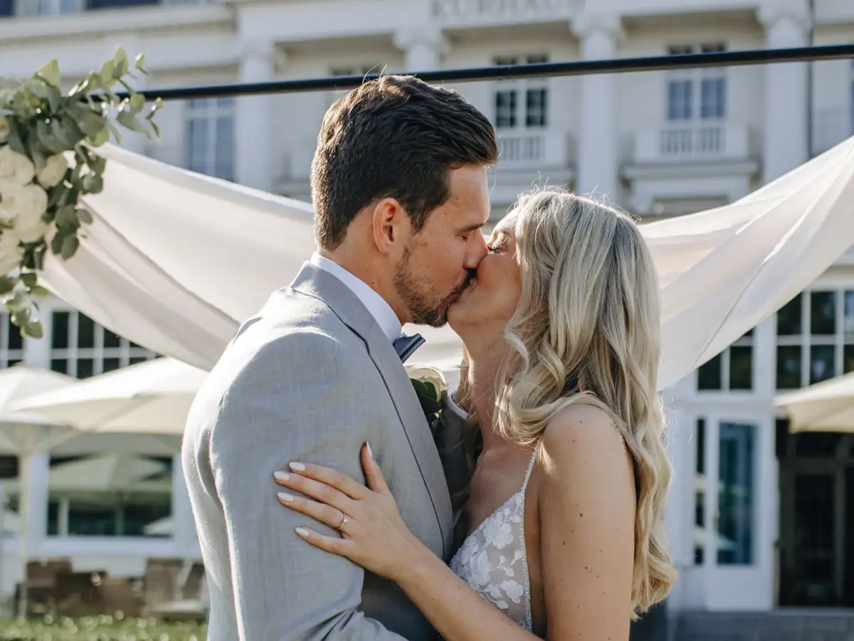 Ein Mann und eine Frau küssen sich im Freien, die Frau trägt ein Hochzeitskleid.