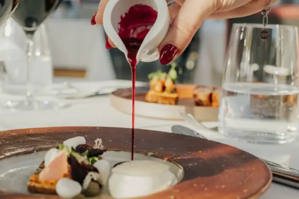 Eine Person gießt rote Sauce auf einen Teller.
