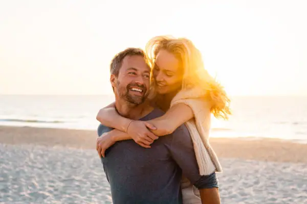 Ein Mann trägt eine Frau auf seinem Rücken am Strand.