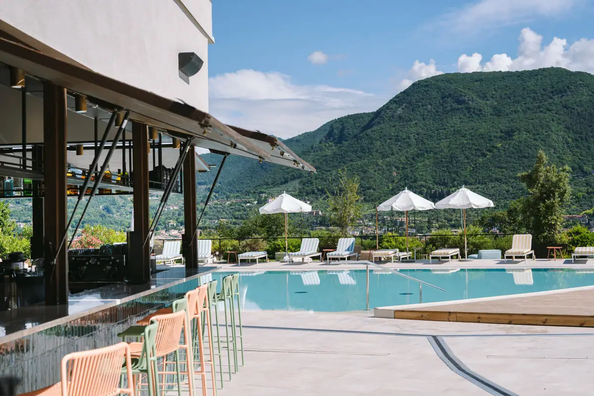 Ein Außenpool mit Sonnenliegen und Sonnenschirmen, im Vordergrund die Poolbar mit bunten Stühlen.