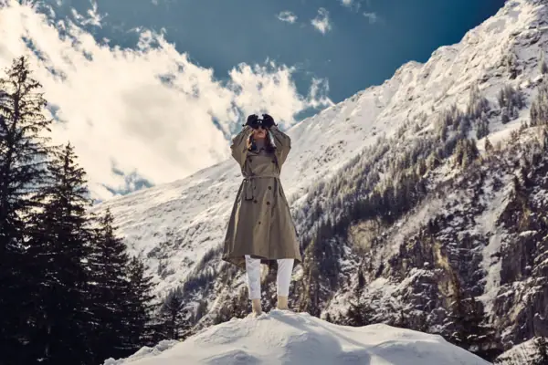 Eine Frau steht auf einem verschneiten Berg mit einem Fernglas.