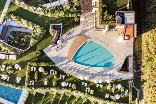 Außenpoolbereich von oben Ein Swimmingpool, umgeben von Rasenflächen und Bäumen.