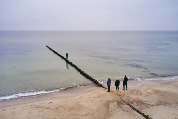 Menschen am Strand mit einem Holzpfosten im Wasser