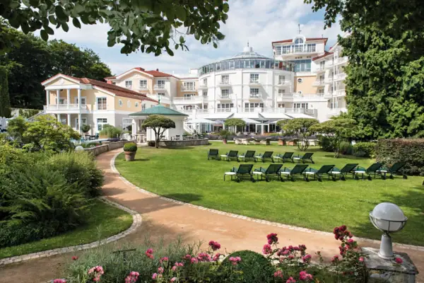 Strandidyll Heringsdorf Liegestühle im Garten mit Rasen und einem Hotel sowie Bäumen im Hintergrund.