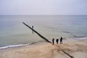 Menschen am Strand mit einem Holzpfosten im Wasser