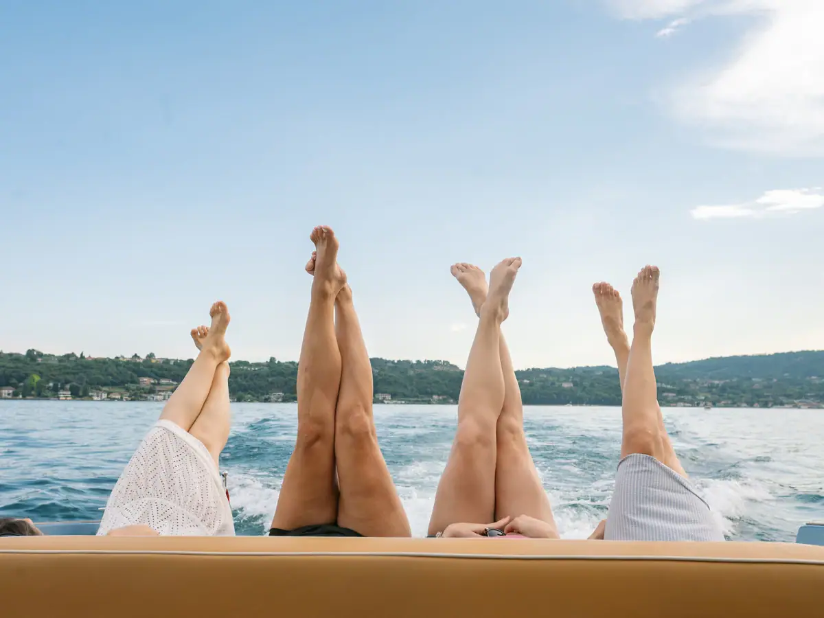 Vier Personen genießen eine entspannte Bootstour auf dem Gardasee und strecken die Beine in die Sonne.
