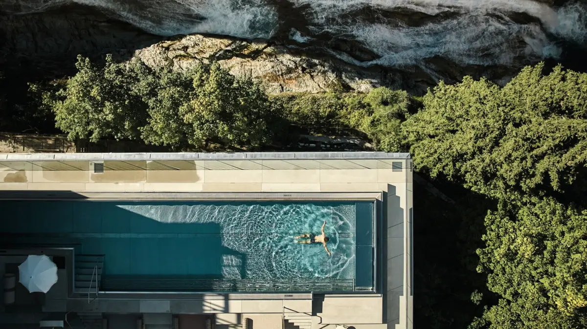 Vogelperspektive eines Poolbildes in dem jemand schwimmt, neben einem Wasserfall, Felsen und Landschaft