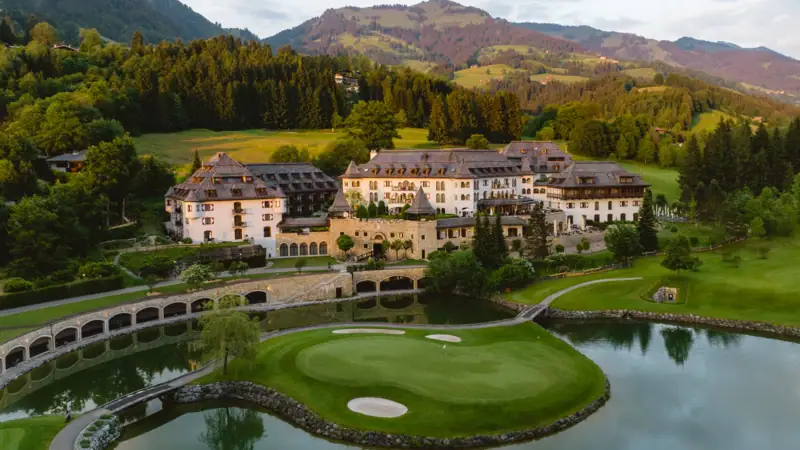 Golfplatz mit großem Gebäude und See im Vordergrund.