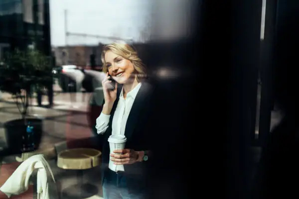 Eine Frau hält eine Kaffeetasse und telefoniert mit einem Handy.