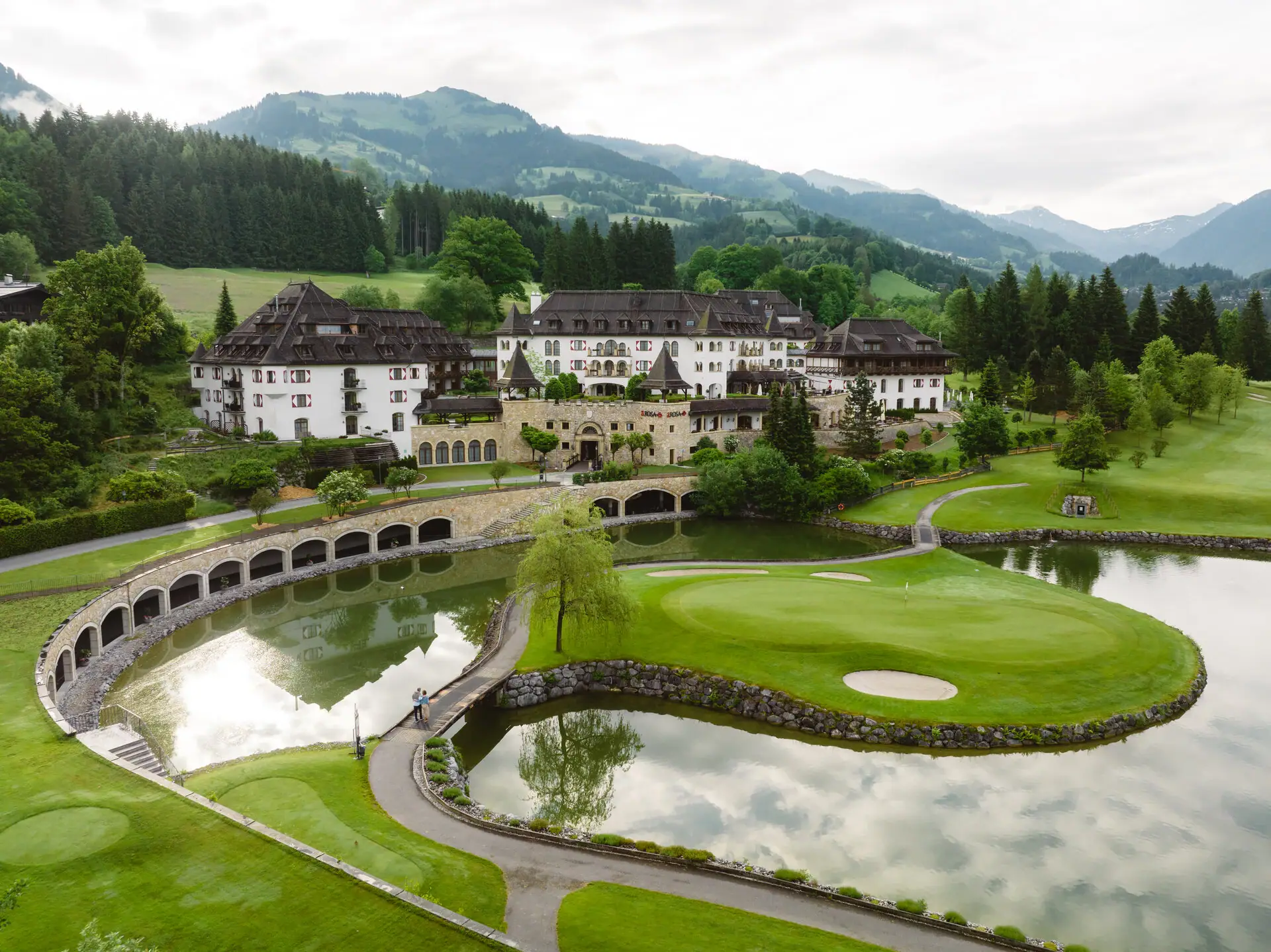 Schlosshotel Kitzbühel Golfplatz mit großem Gebäude und einem See im Vordergrund