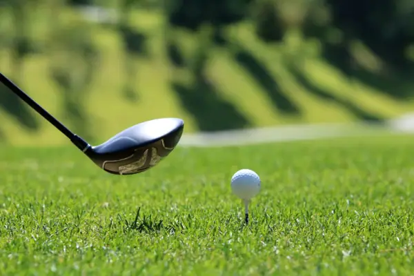 Ein Golfschläger und ein Golfball auf einem Tee im Gras.