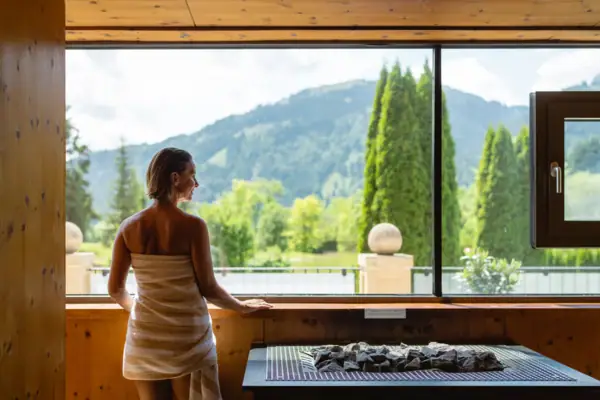 Eine Frau steht vor einem Fenster und blickt auf einen Berg.