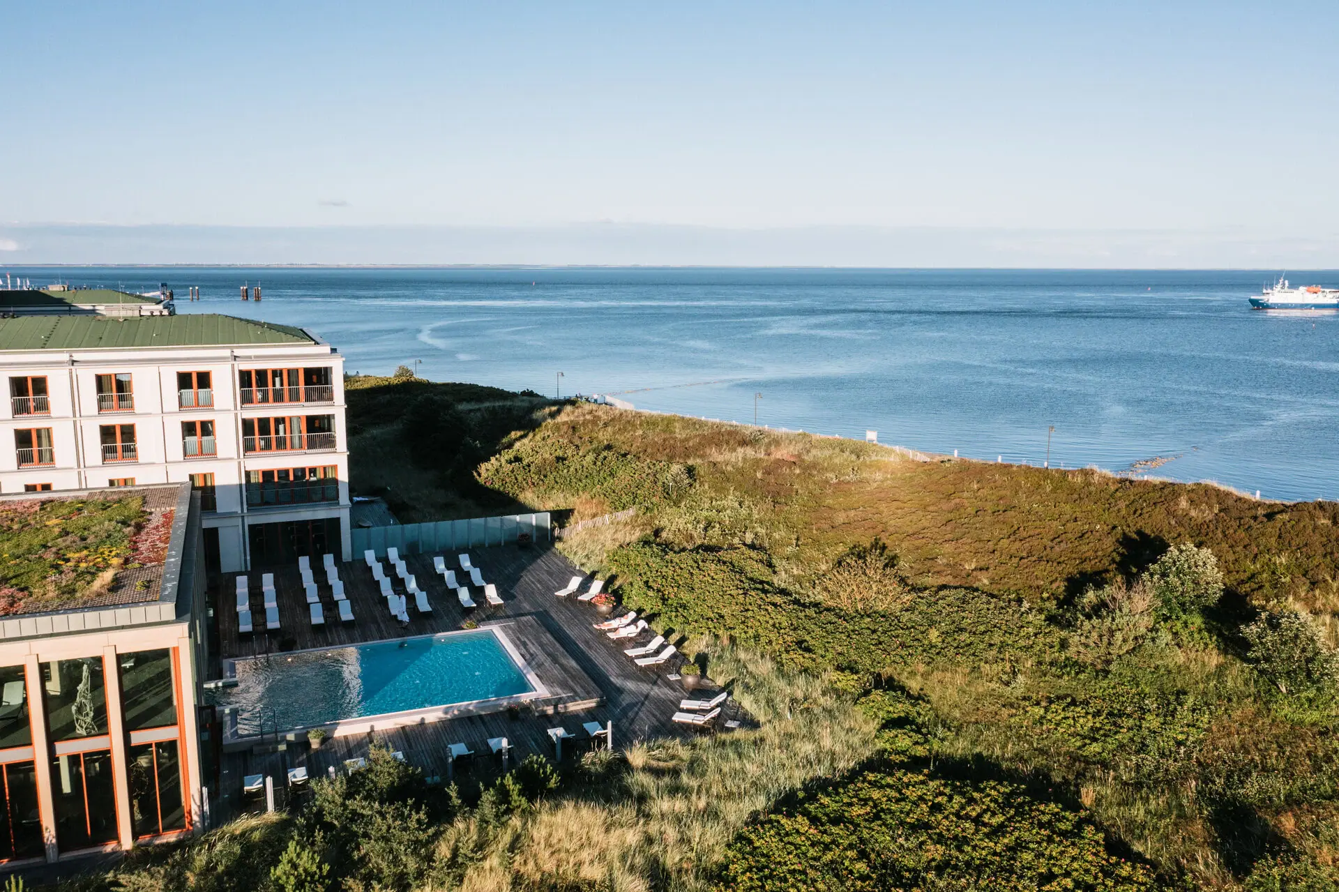 Ein Außenpool vor einem Gebäude mit Blick auf das Meer im Hintergrund.