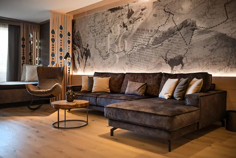 Wohnbereich einer Suite im Ifen Hotel Kleinwalsertal Gemütliches Wohnzimmer im alpinen Stil mit vielen Holzelementen, alpinen Details, kunstvoll gestalteter Tapete, Couch und Tisch.
