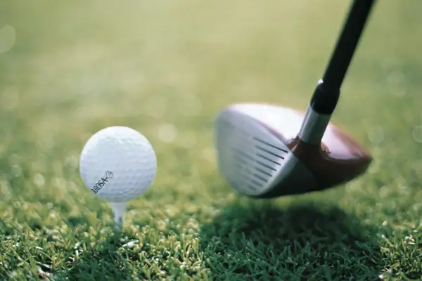 Ein Golfball auf einem Tee mit einem Golfschläger daneben auf einer Rasenfläche.