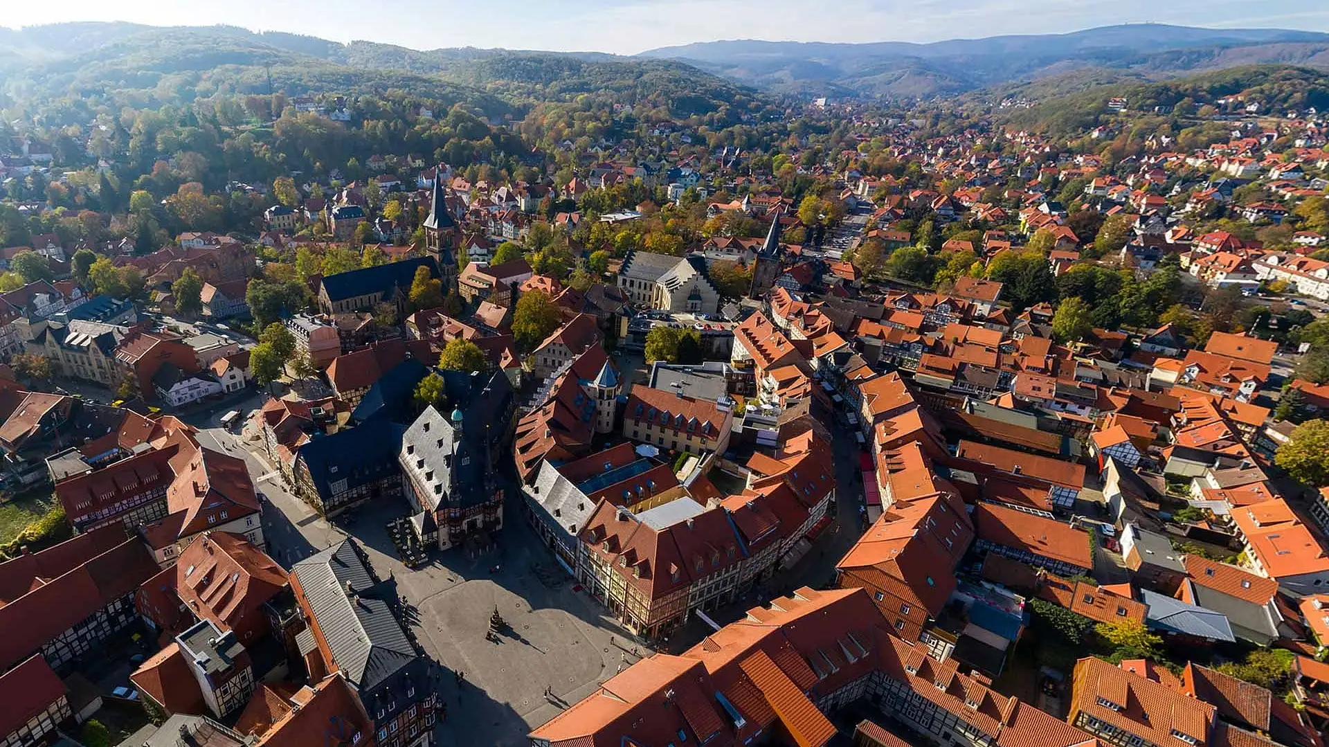Luftaufnahme einer Stadt mit Häusern, Bäumen und Bergen im Hintergrund.