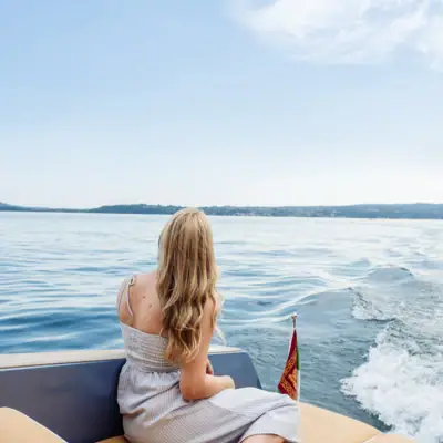 Aktivitäten Eine Frau sitzt auf einem Boot. Das Boot fährt auf dem Gardasee. Die Frau schaut in die Ferne.