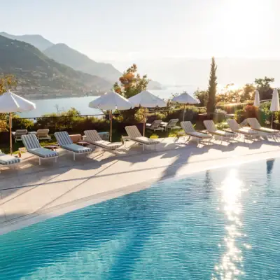 Wellness Ein Außenpool mit Liegestühlen und Sonnenschirmen vor einem See im Hintergrund.