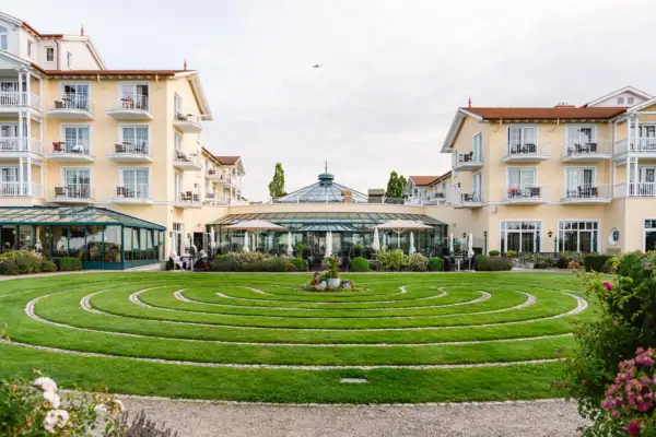 Ein kreisförmiges Labyrinth in einem grasbewachsenen Bereich mit Gebäuden im Hintergrund.