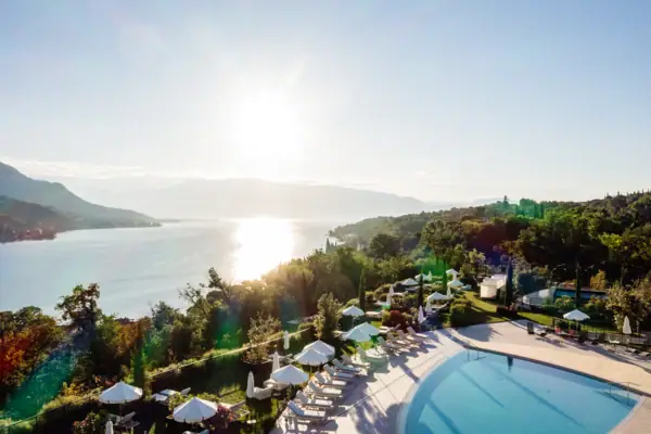 Außenpool vom A-ROSA Gardasee Drohnenaufnahme vom Pool mit Sonnenschirmen und Liegestühlen dahinter der Blick auf den Gardasee.