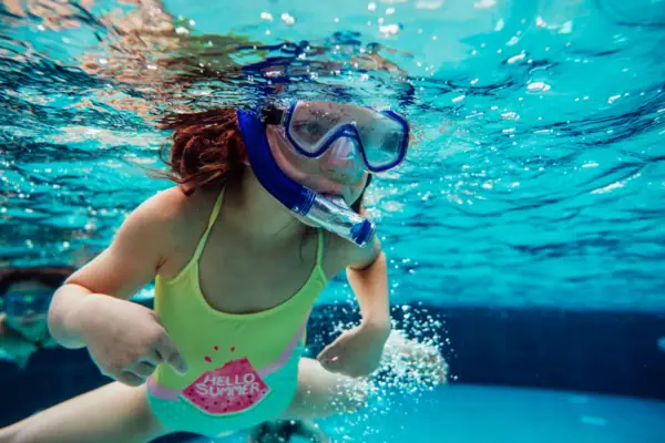 Ein Mädchen mit Taucherbrille schnorchelt unter Wasser.