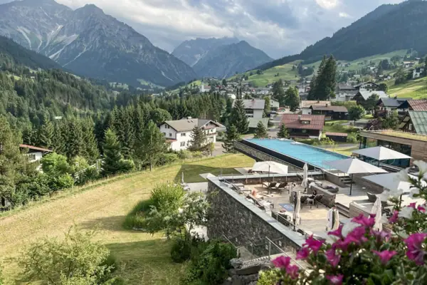 A-ROSA Ifen Hotel Kleinwalsertal Ein Pool vor einem Gebäude mit Bergen im Hintergrund.