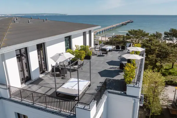 A-ROSA Ceres am Meer Ein Gebäude mit einer Terrasse und Sonnenschirmen mit Blick auf das Wasser.