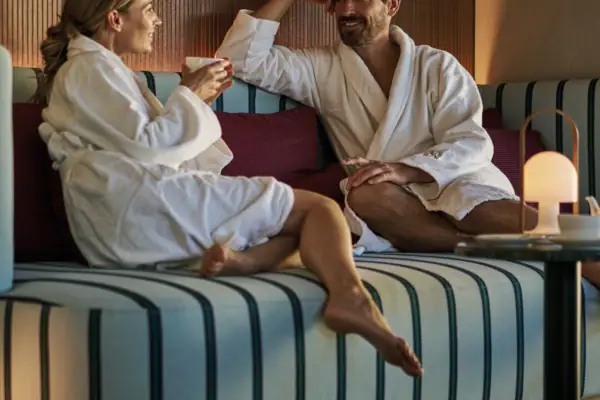 Ein Mann und eine Frau in Bademänteln sitzen auf einem Sofa.