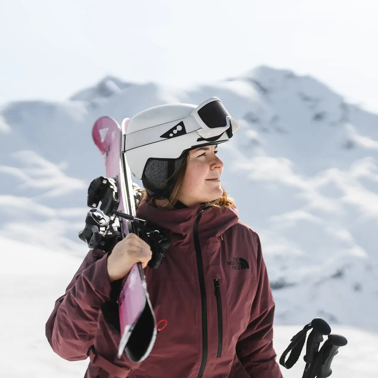 Frau hält Ski und Stöcke im Freien auf verschneitem Gelände.