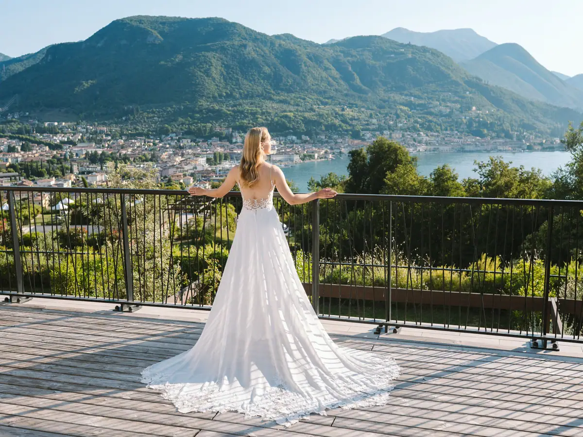 Eine Frau in einem weißen Brautkleid steht auf der Terrasse der A-ROSA Suite mit Blick auf den Gardasee.
