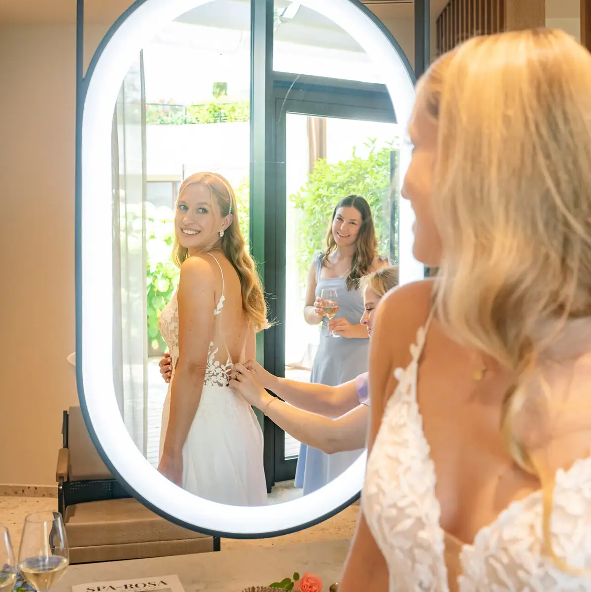 Braut wird von Freundinnen beim Anziehen des Hochzeitskleids im A-ROSA Gardasee unterstützt.