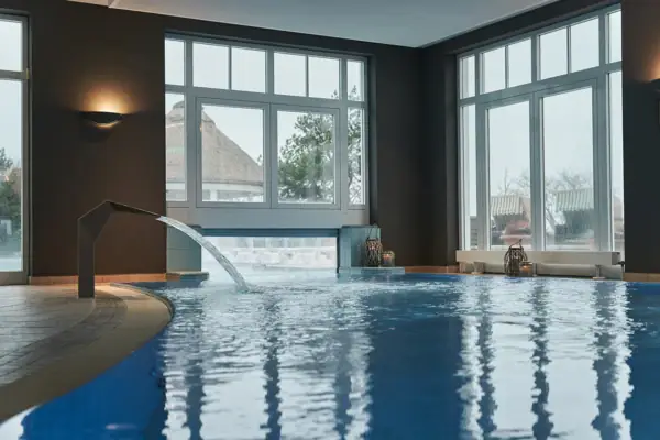 Ein Hallenbad mit Wasserfall und großen Fenstern.