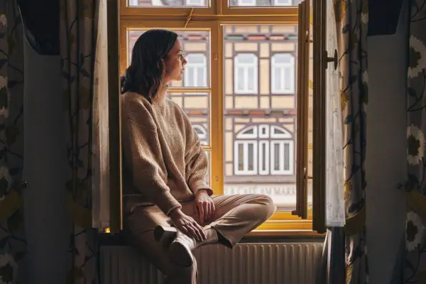 Eine Frau sitzt auf einer Fensterbank und schaut aus dem Fenster.