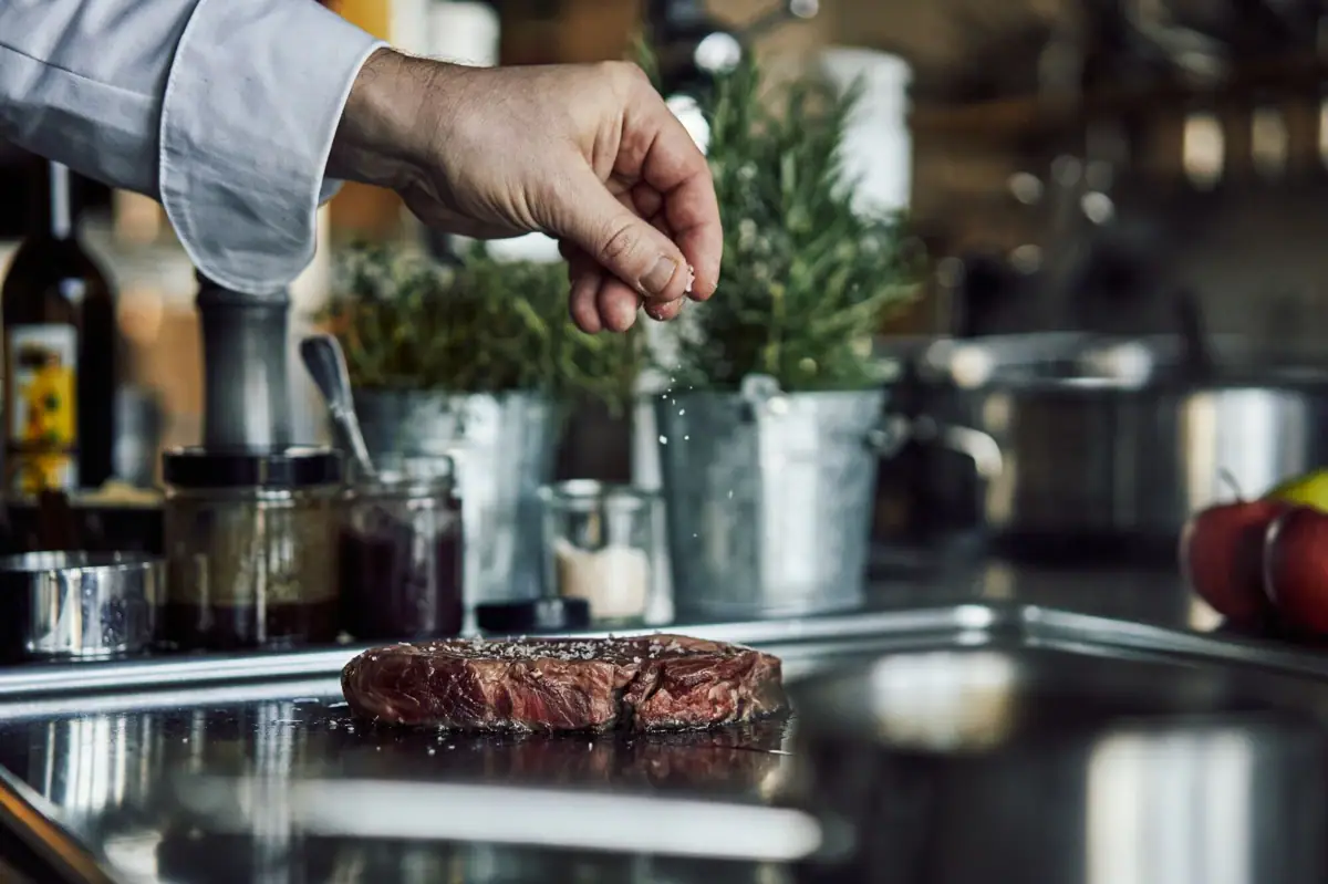 Eine Hand streut Salz auf ein Stück Fleisch.