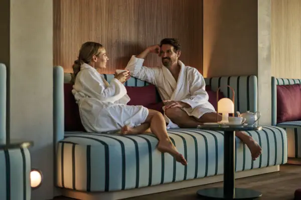 Paar im SPA-ROSA Ein Mann und eine Frau in Bademänteln sitzen auf einem Sofa.