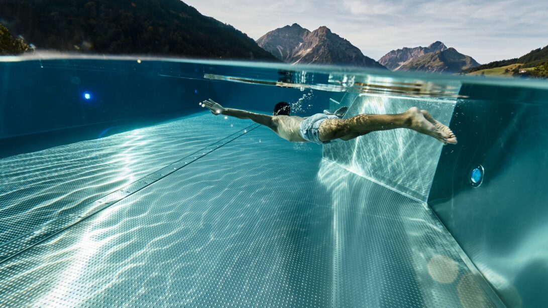 Mann taucht im Pool und in der Ferne ist eine Berglandschaft zu erkennen