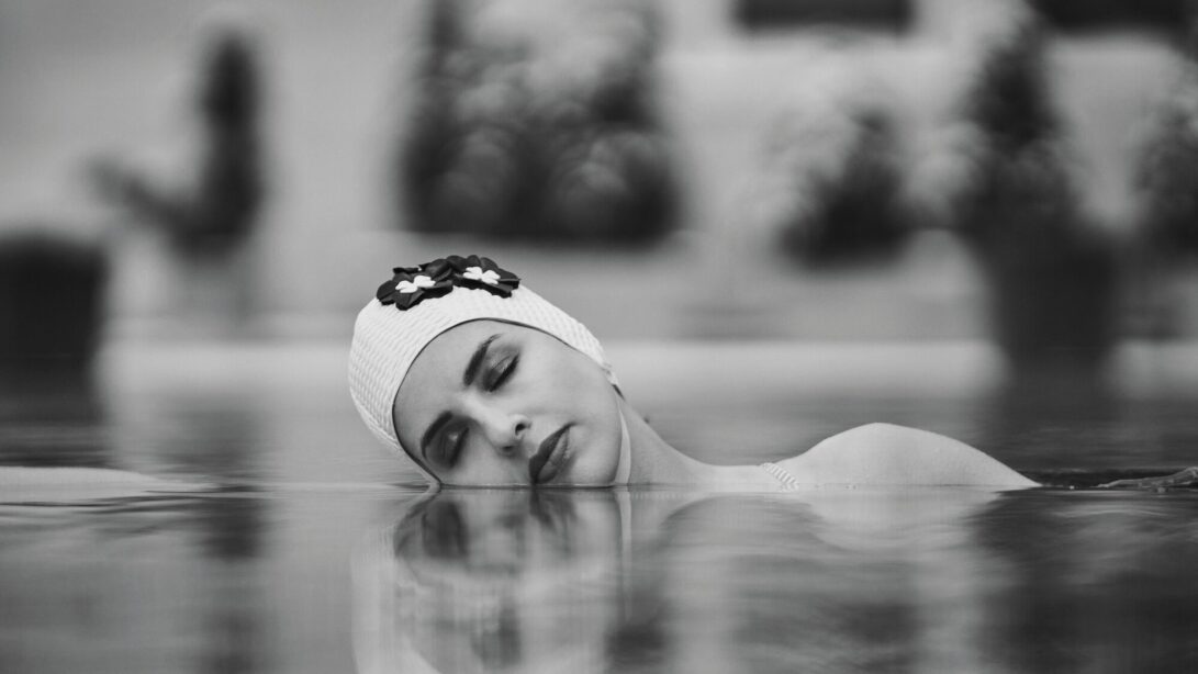 Frau liegt mit Kopf geneigt im Wasser und trägt dabei eine Badekappe mit Blumen