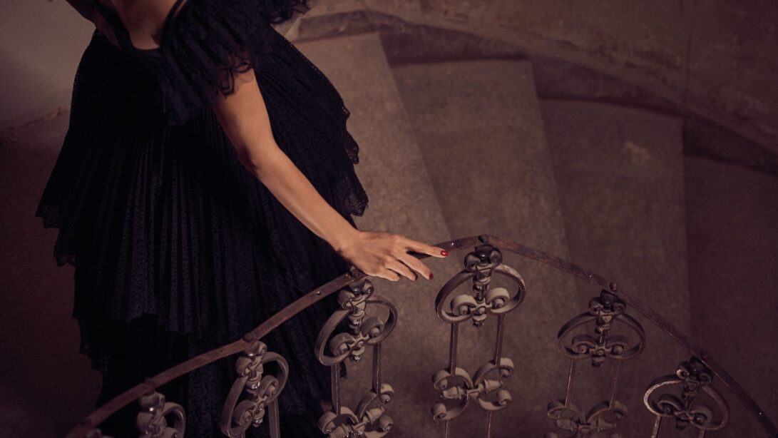 Frau im schwarzen Abendkleid berührt Treppengeländer einer Wendeltreppe