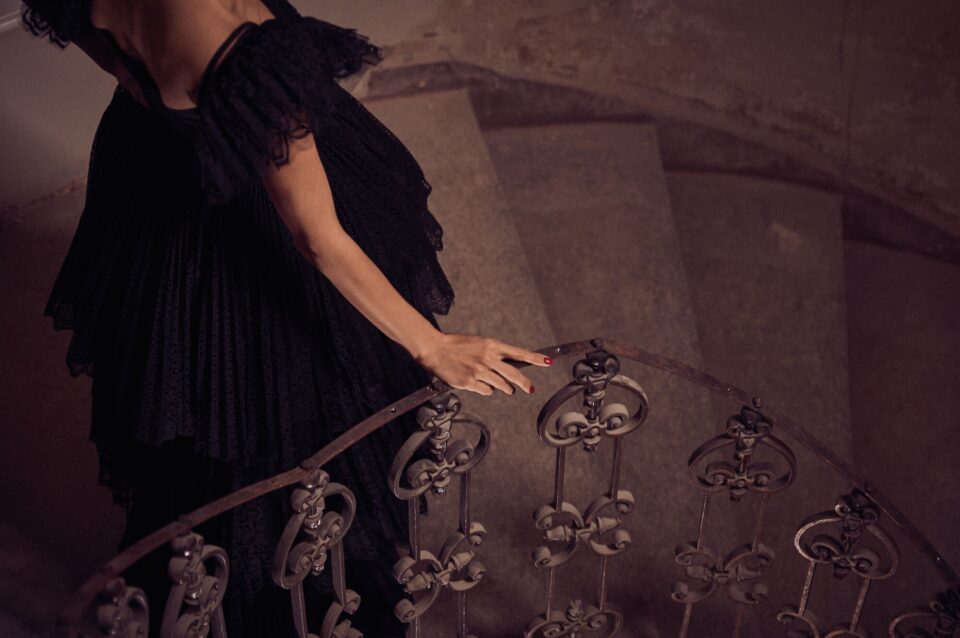Frau im schwarzen Abendkleid berührt Treppengeländer einer Wendeltreppe
