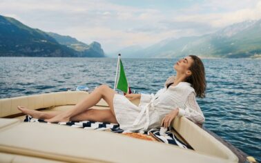 Frau liegt entspannt im weißen Blusenkleid auf deinem Boot auf dem Gardasee