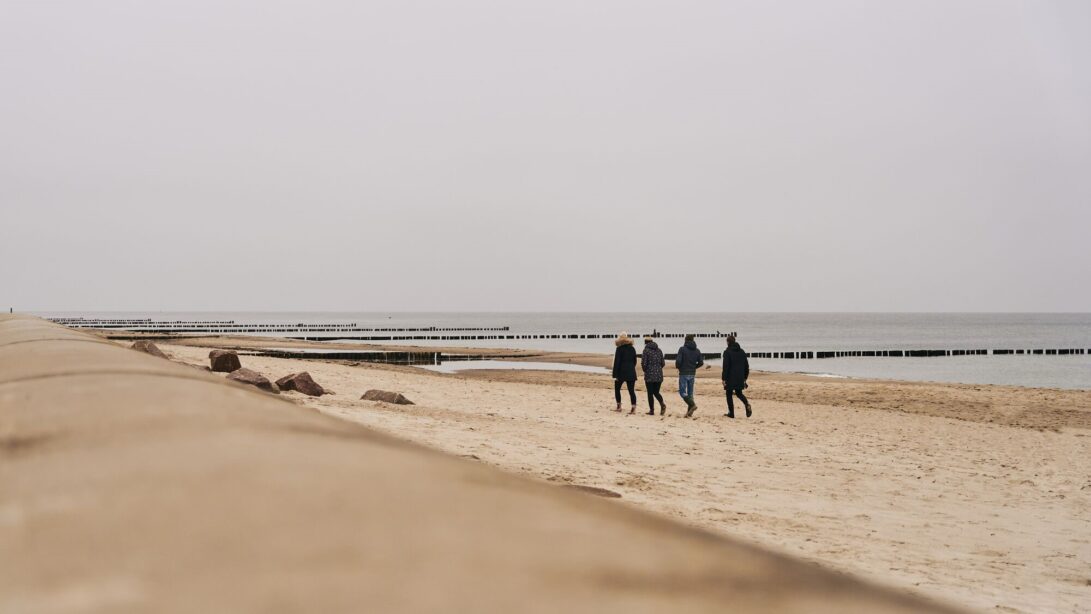 Gruppe von vier Personen spaziert warm angezogen über den Strand an der Ostsee in Kühlungsborn