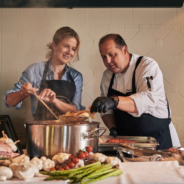 Ein Mann und eine Frau mit einer Schütze stehen in einer Küche vor einem Kochtopf und Kochen Krustentiere im Ostseehotel.