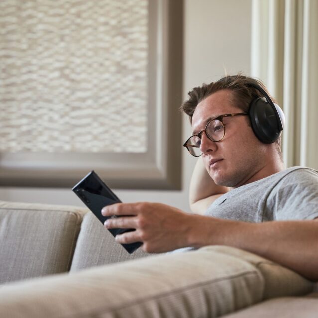 Mann hört Podcast auf Sofa mit Kopfhörern und schaut auf sein Handy
