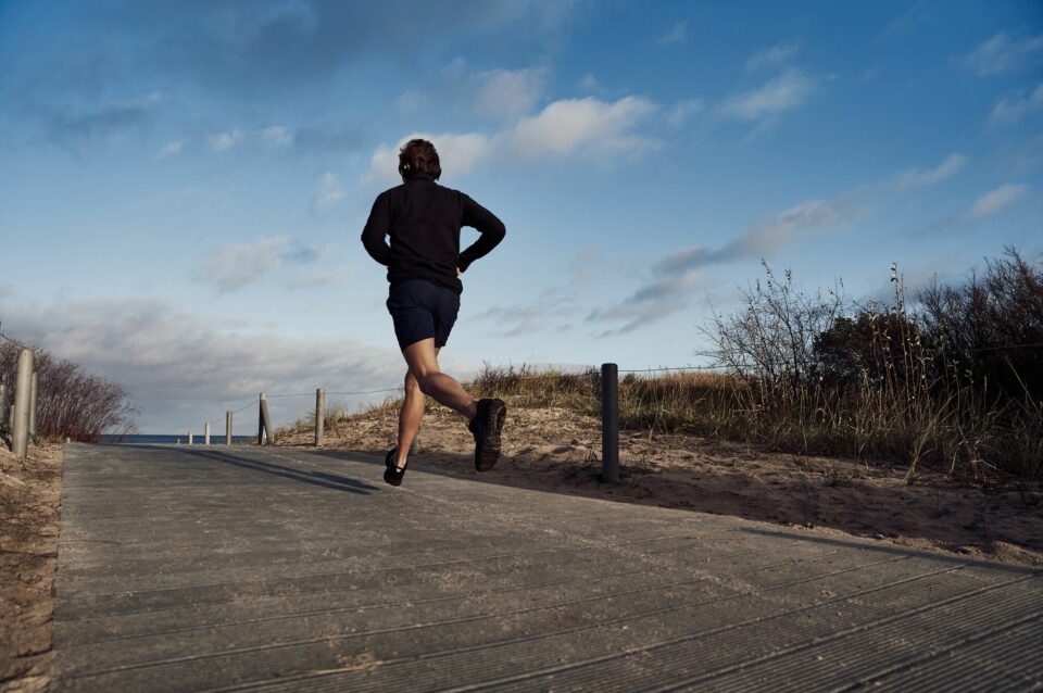Ein Mann joggt auf einem leeren Weg in Richtung Meer. Im Hintergrund ist ein leicht bewölkter blauer Himmel.