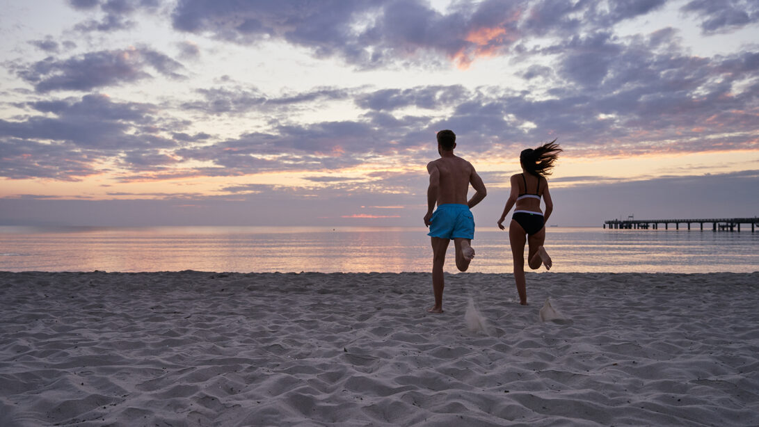 Frau und Mann laufen in Badebekleidung im Sonnenuntergangauf das Meer zu