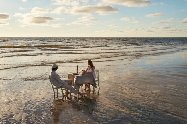 Paar sitzt am Esstisch direkt am Strand beim Sonnenuntergang