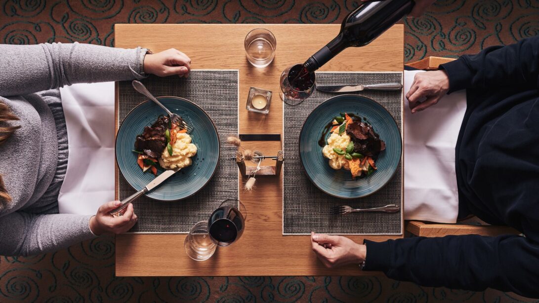 Paar sitzt am gedeckten Restauranttisch und Kellner schenkt Wein nach